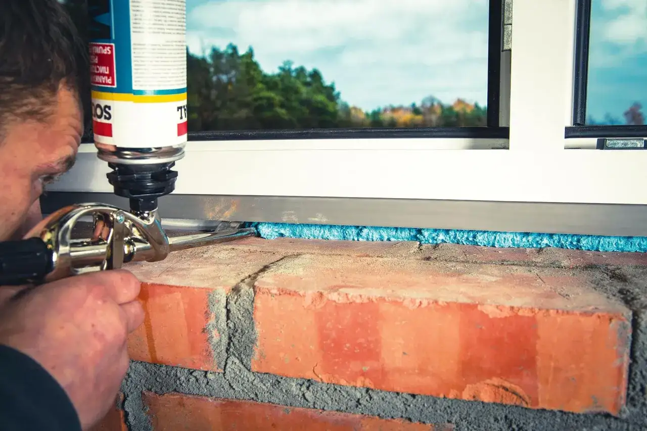 Montaż okna: pianka wypełnia szczelinę między cegłą a ramą. Kluczowe jest ile cm pianki przy montażu okien, by zapewnić izolację.