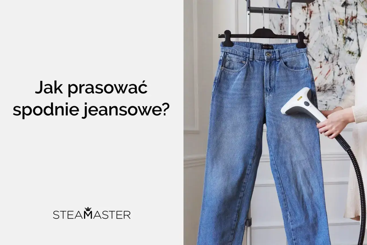 Dłoń trzymająca parownicę prasuje dżinsowe spodnie wiszące na wieszaku.