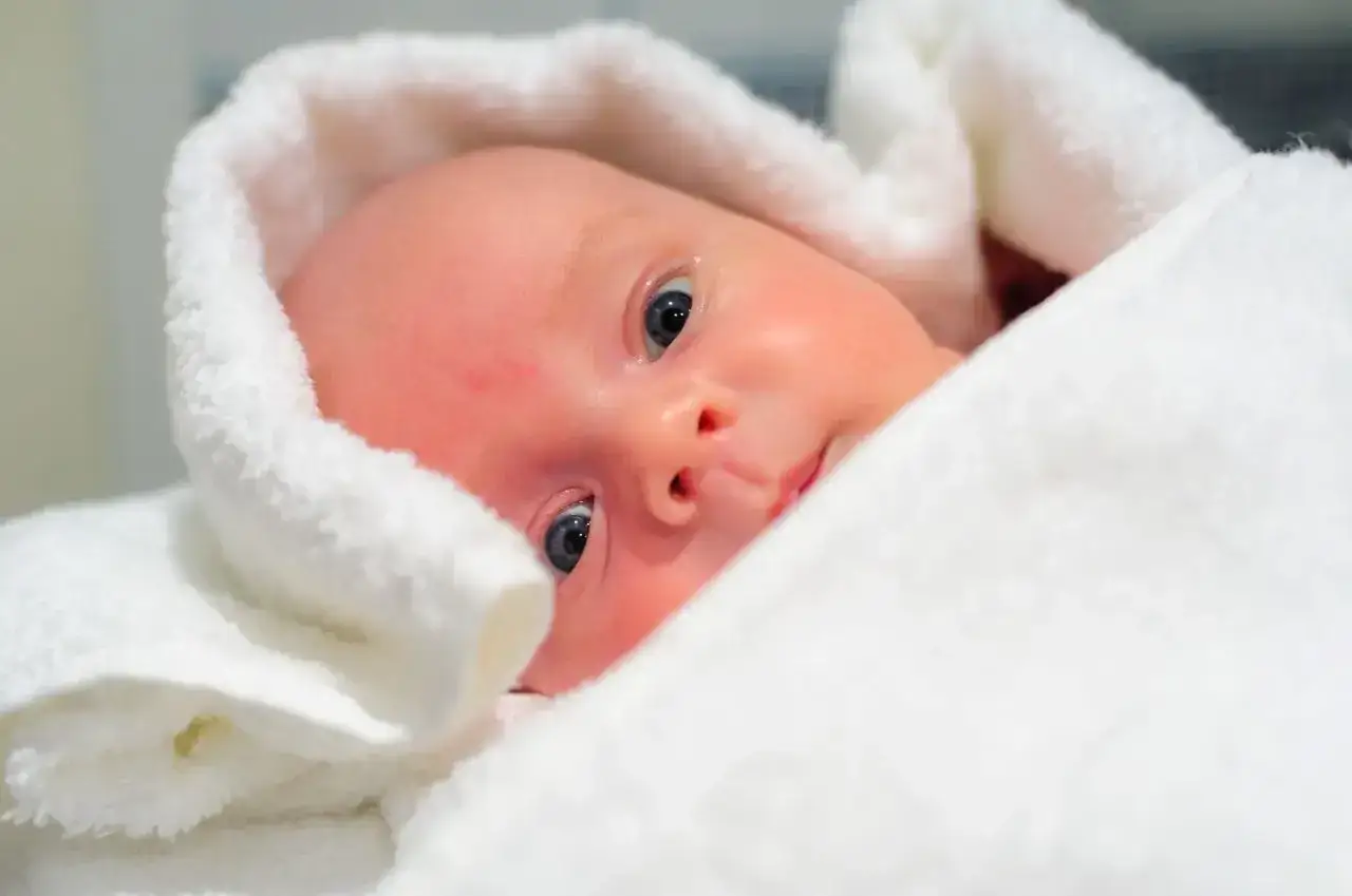 Noworodek wtulony w biały ręcznik, patrzący w obiektyw.