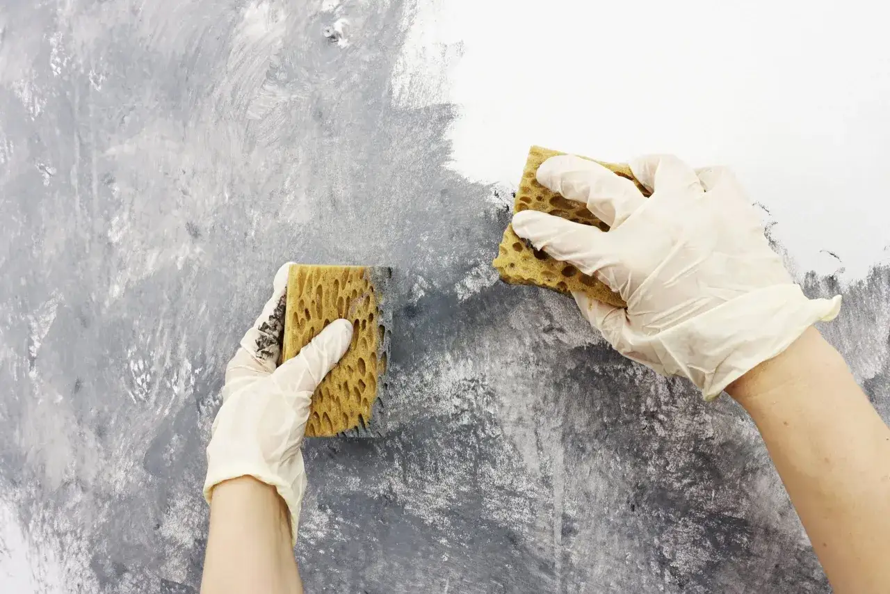 Ręce w rękawiczkach tworzą na ścianie ciekawe wzory, używając gąbek do malowania.