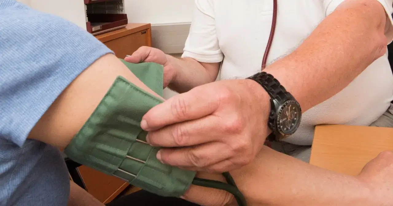 Lekarz zakłada mankiet do pomiaru ciśnienia krwi. Wartości prawidłowe mogą się różnić w zależności od wieku, dlatego ważna jest cisnienie krwi tabela wiekowa.