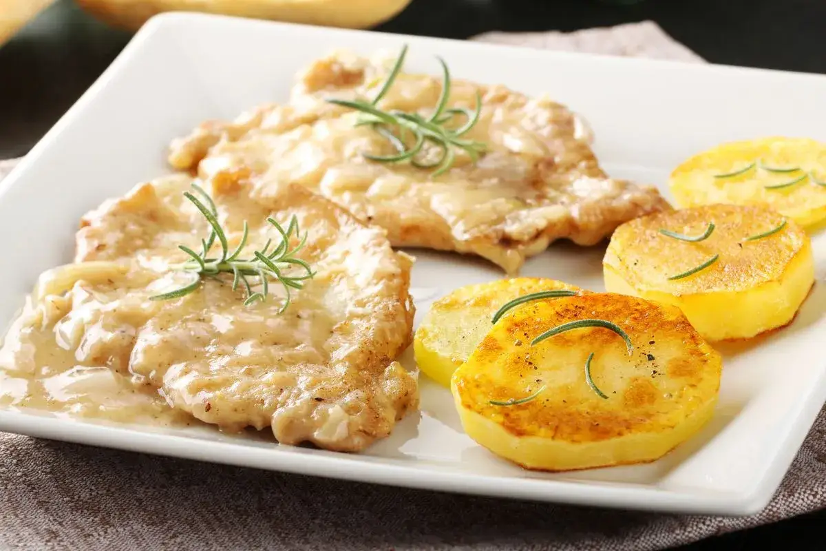 Two breaded chicken cutlets in creamy sauce with rosemary, served with pan-fried potato slices.