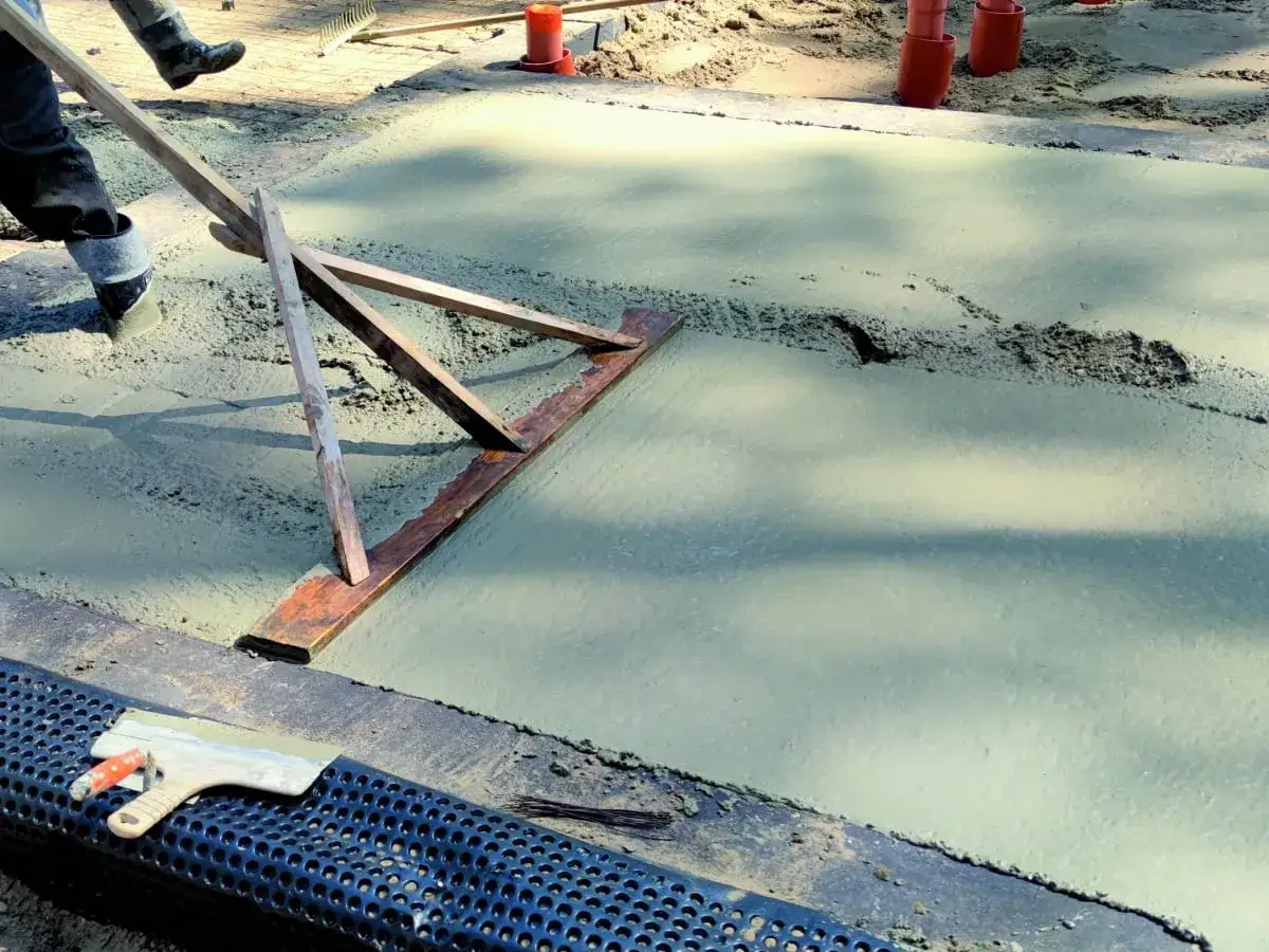 Pracownik wyrównuje świeży beton, sprawdzając, jaka grubość chudziaka jest potrzebna. Narzędzie do zacierania betonu w akcji.