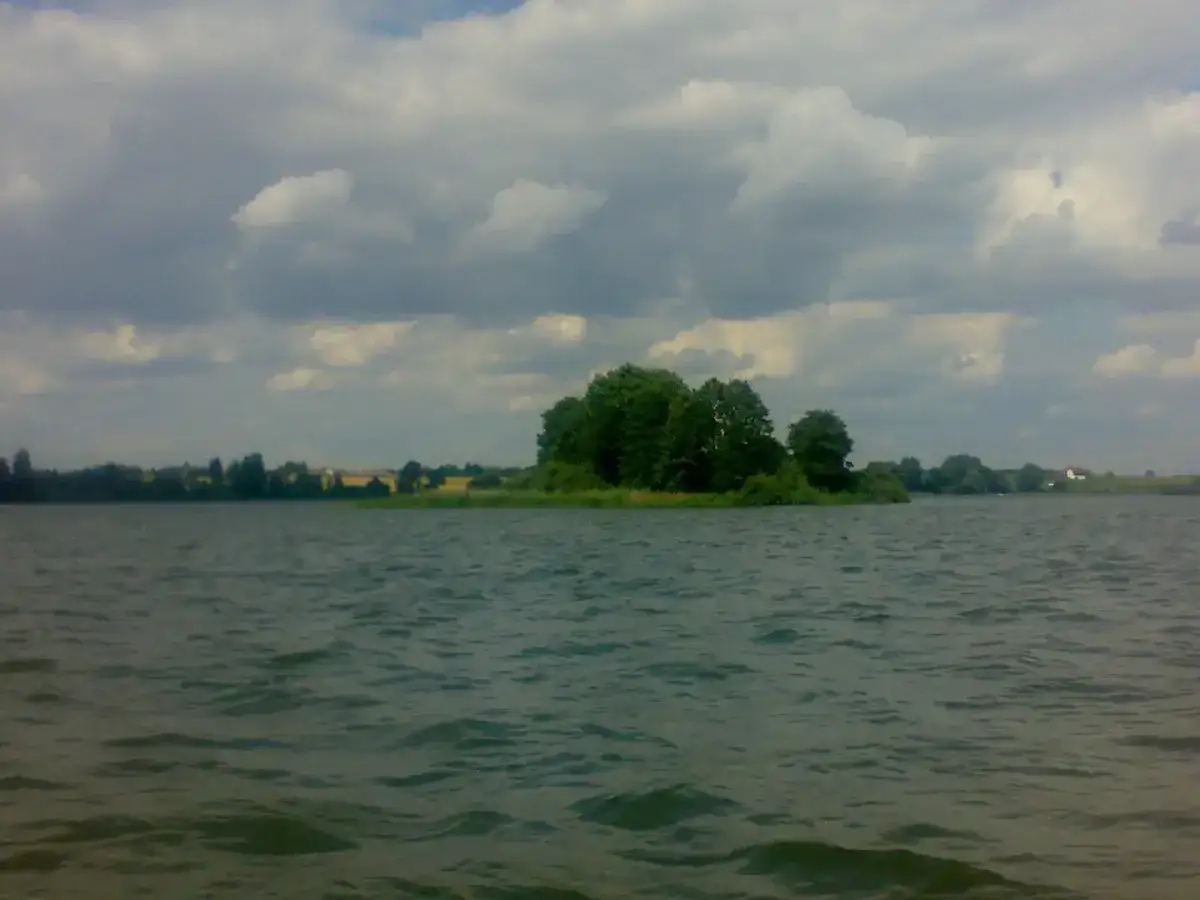 Spokojne jezioro Głuszyńskie, idealne na wędkowanie. Na horyzoncie zielone drzewa i chmury.