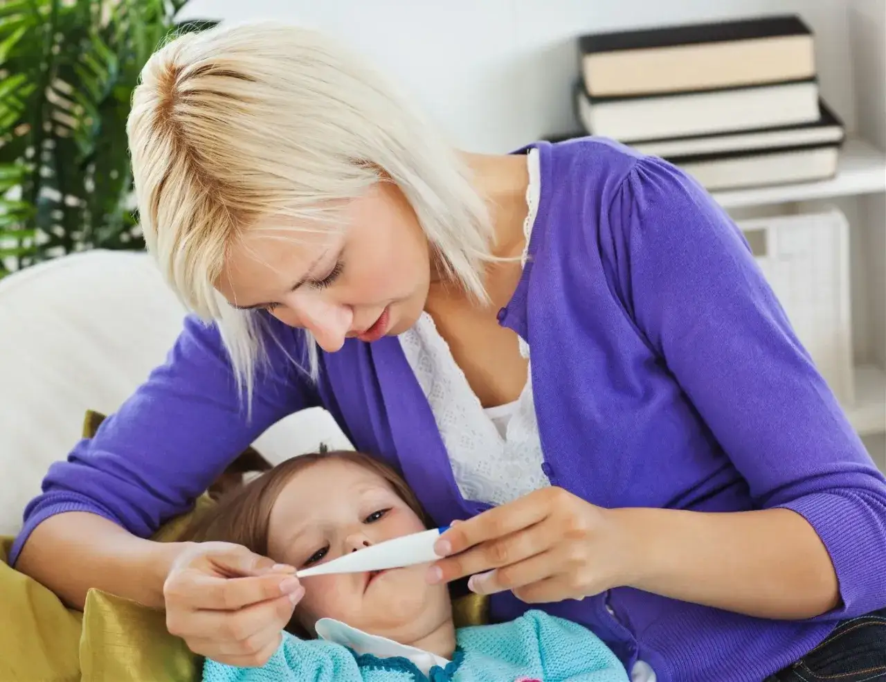 Zmartwiona mama mierzy temperaturę choremu dziecku. Warto wiedzieć, czy można kąpać dziecko z gorączką.
