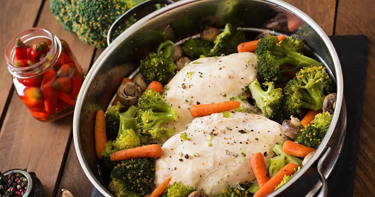 Dwa filety z kurczaka z brokułami, marchewką i pieczarkami w garnku. Czy brokuły są lekkostrawne? Tak, gotowane są łatwe do strawienia.
