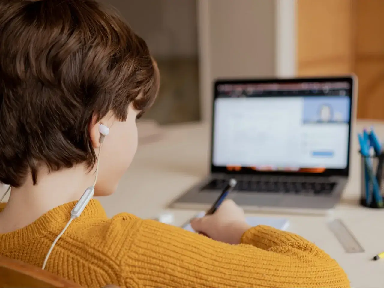 Chłopiec w żółtym swetrze uczy się zdalnie, pisząc notatki. Czy uczniowie dostaną laptopy, by móc tak pracować?