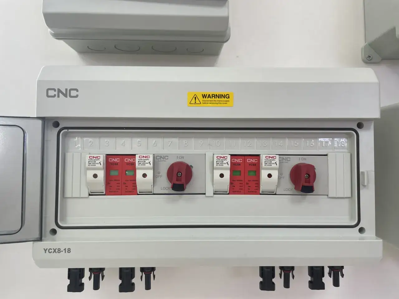 Biała skrzynka elektryczna z czerwonymi przełącznikami i numerowanymi slotami.