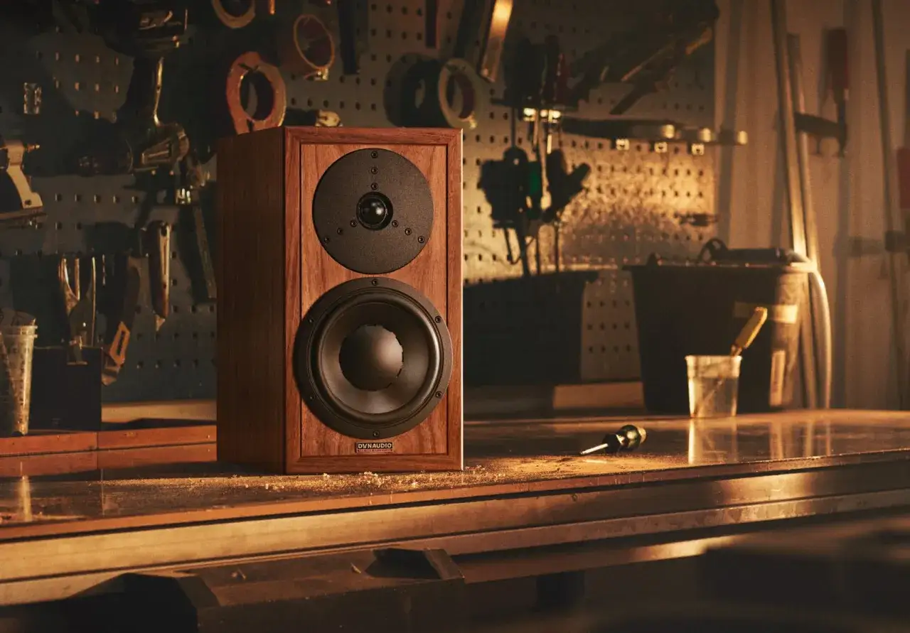 Głośnik Dynaudio Special 25 w drewnianej obudowie, stojący na stole w warsztacie, otoczony narzędziami.