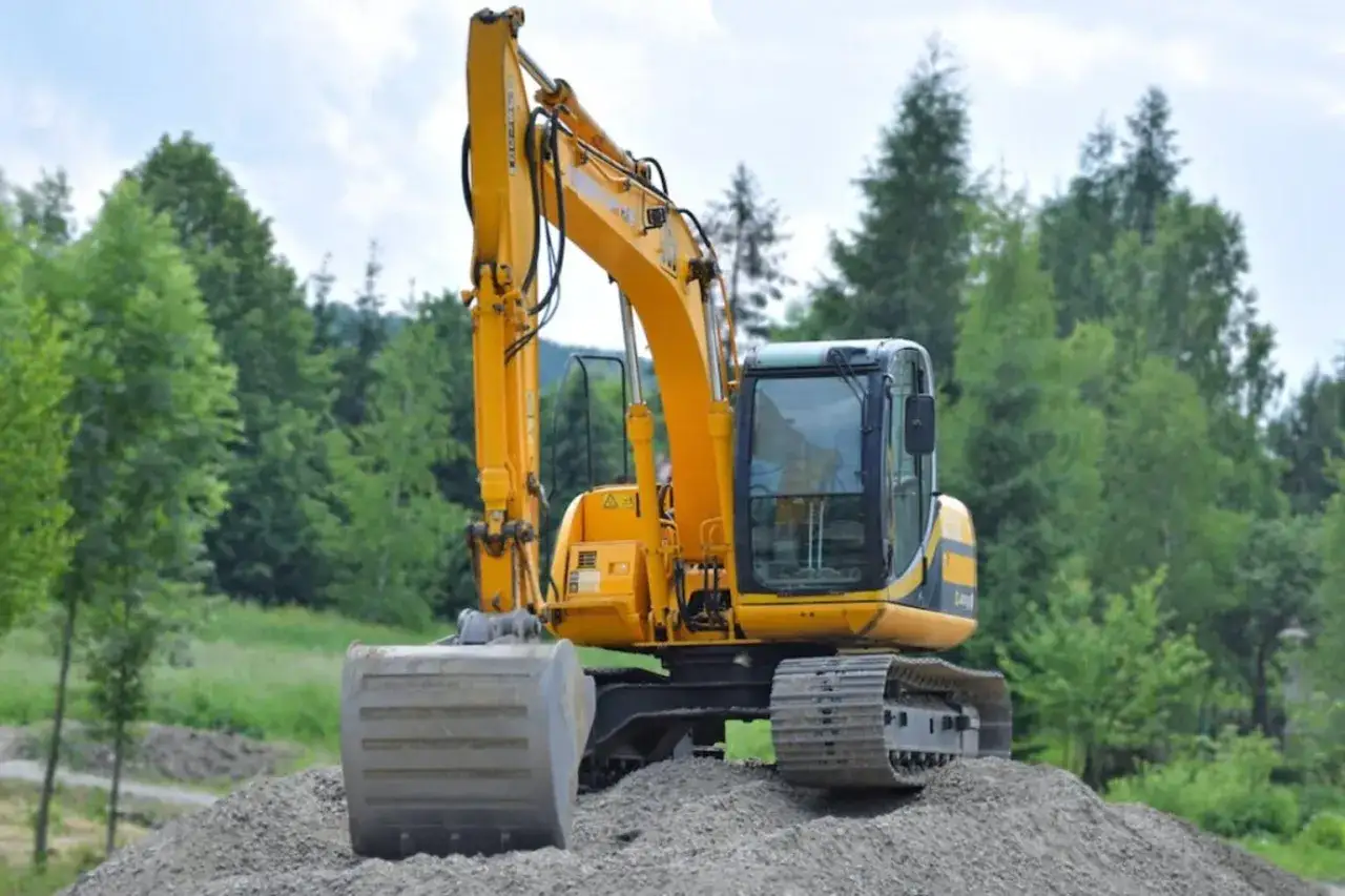 Żółta koparko-ładowarka na placu budowy, gotowa do egzaminu na koparko ładowarki. W tle las.