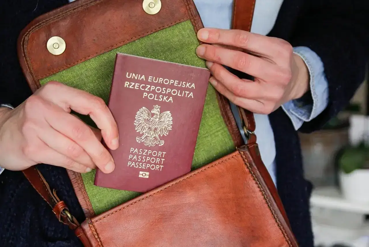 Dłonie wkładają polski paszport do brązowej torby. Czy na paszport można wziąć kredyt? To pytanie, które może pojawić się przy planowaniu podróży.