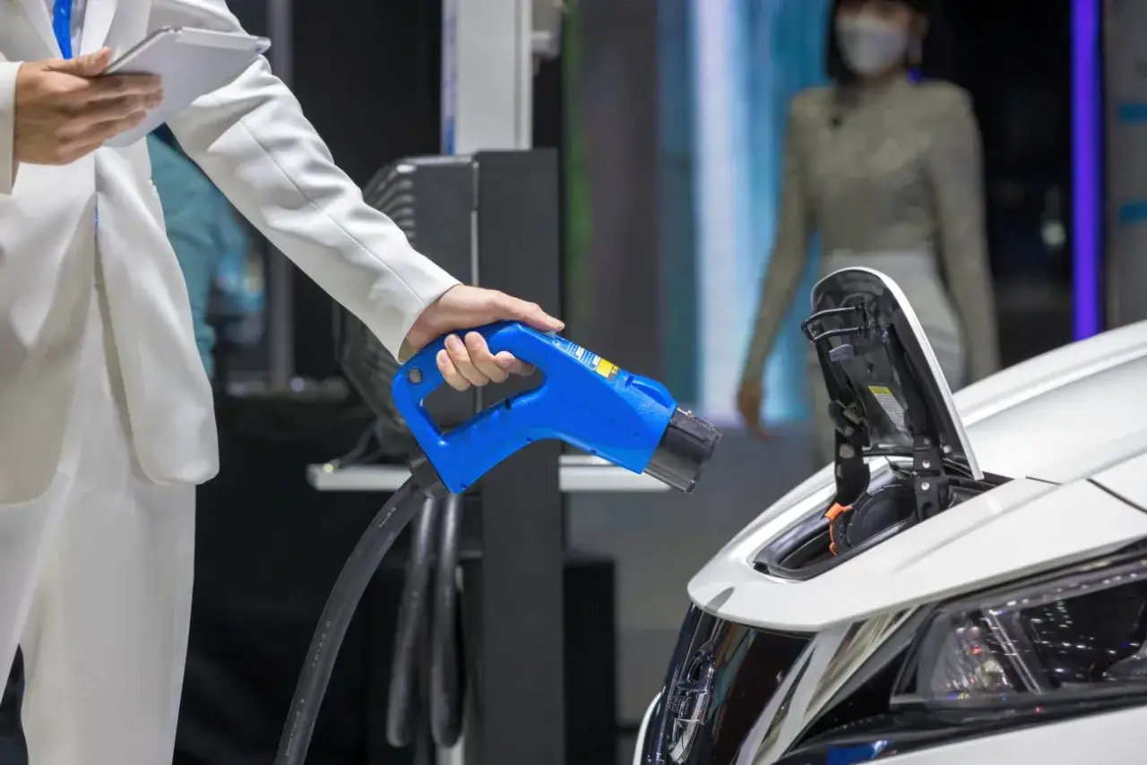 Elektromobilność w zamówieniach publicznych: ładowanie pojazdu elektrycznego. Dłoń trzymająca niebieską wtyczkę ładowarki.