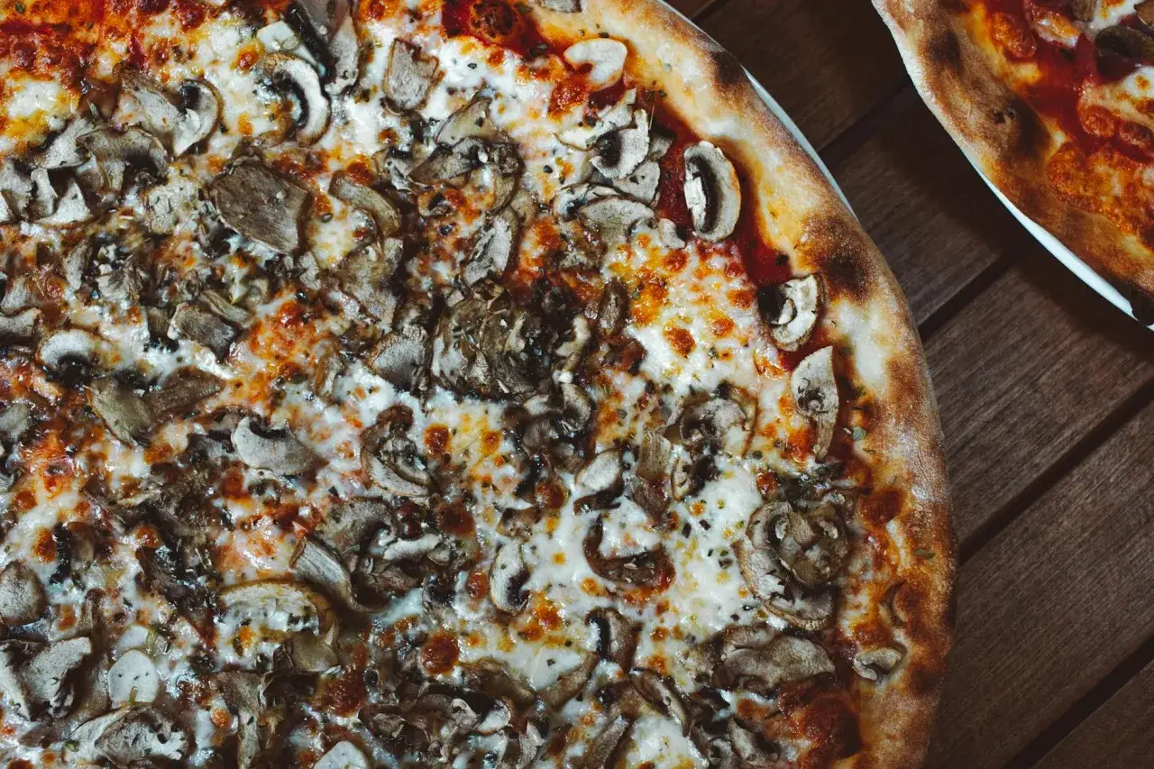 Pyszna pizza wegetariańska z pieczarkami i ciągnącym się serem, idealna na wspólny wieczór.