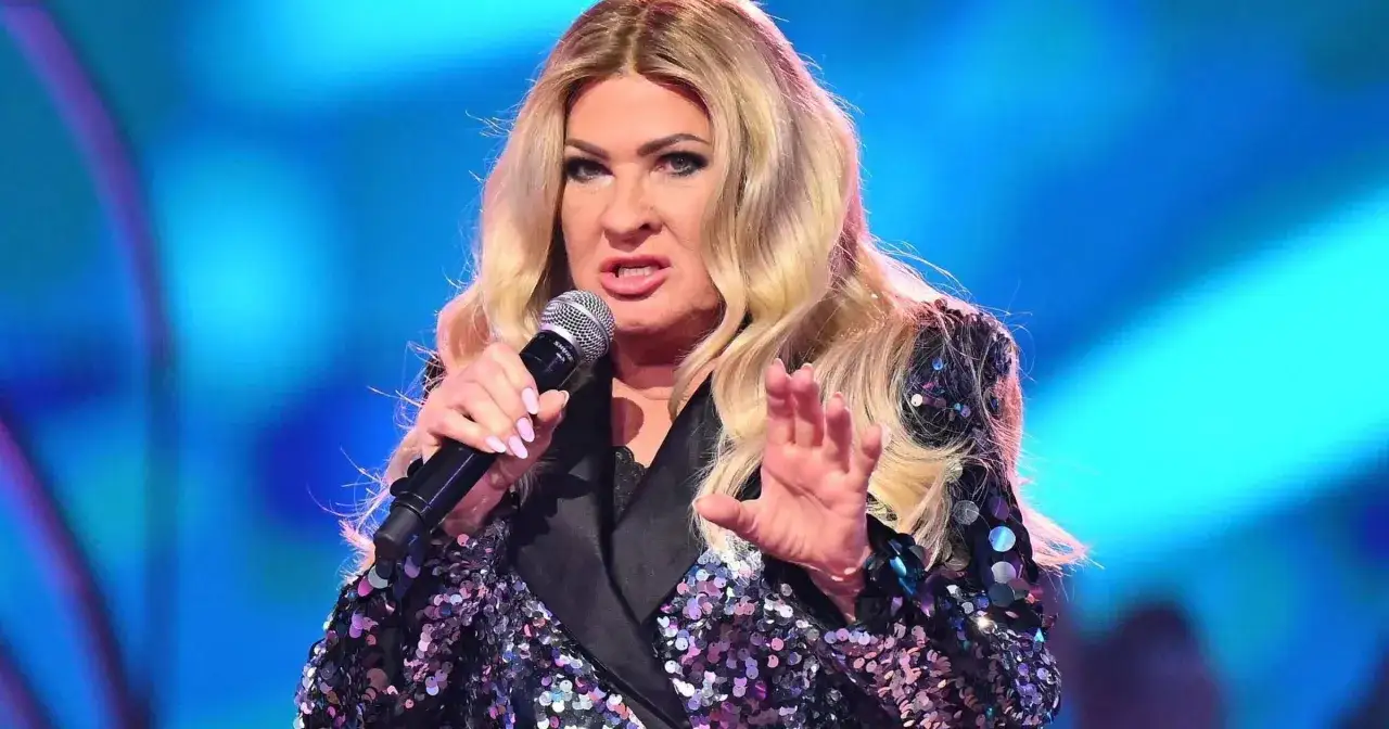 Beata Kozidrak w cekinowej marynarce śpiewa do mikrofonu na tle niebieskiego światła.