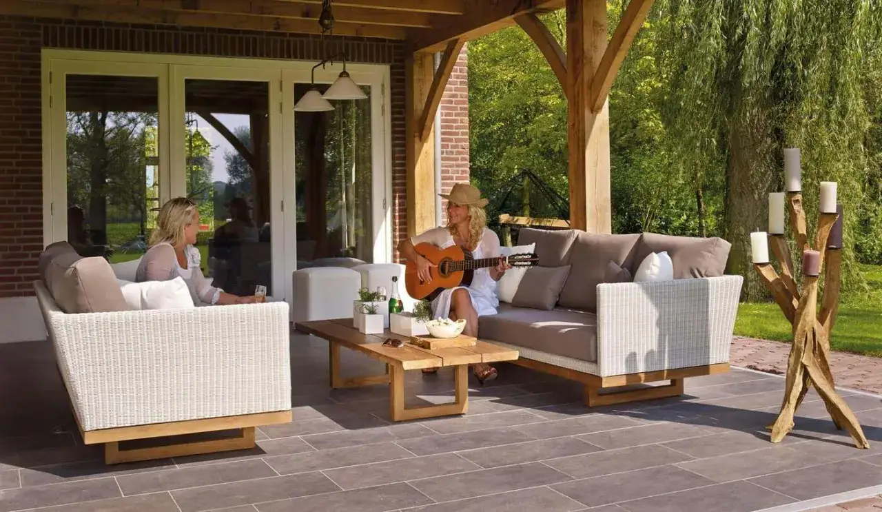 Kobieta gra na gitarze na tarasie, siedząc na sofie obok koleżanki. To idealne miejsce na relaks, jakby to był prywatny balkon.