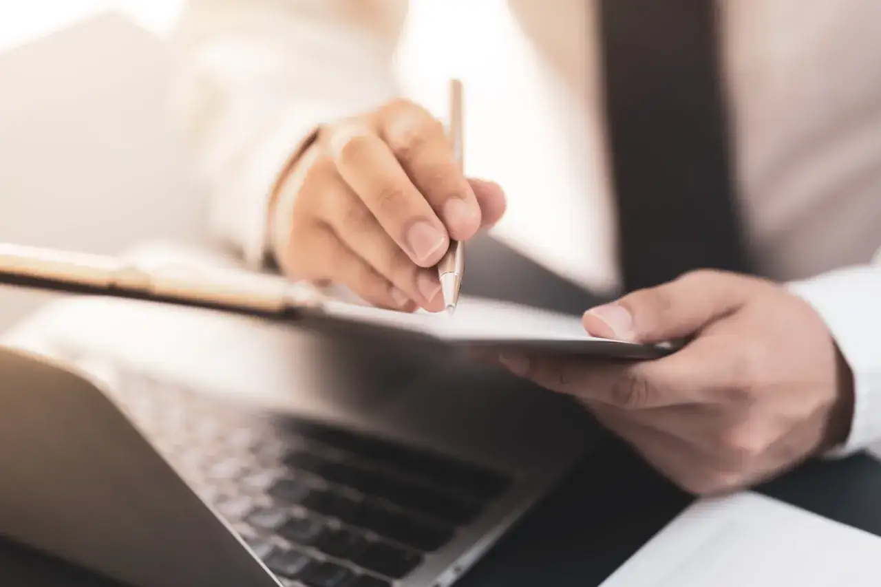 Dłoń trzymająca długopis nad dokumentem, analizująca wskaźnik rentowności majątku.