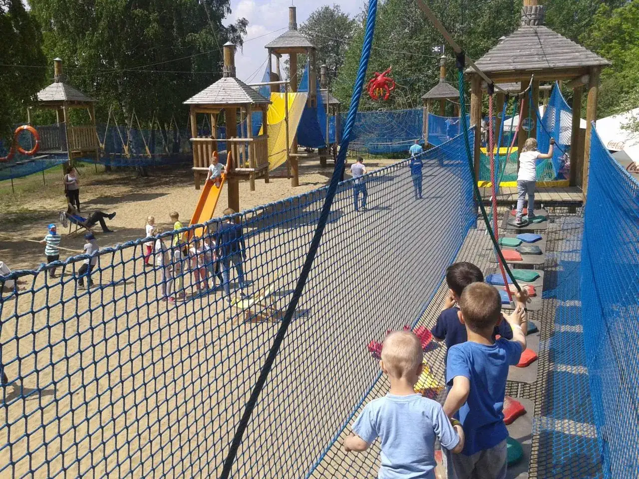 Dzieci bawią się na placu zabaw w parku linowym, pokonując przeszkody.