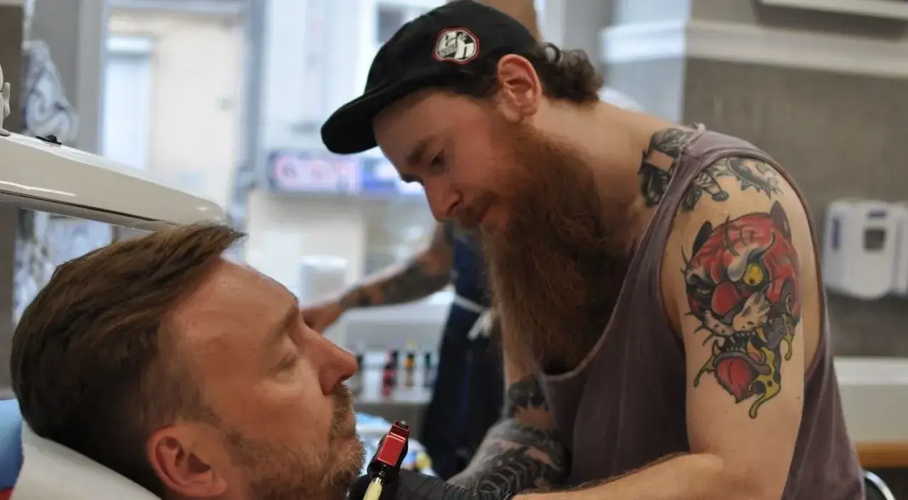 Artysta z tatuażem tygrysa na ramieniu wykonuje nowy wzór. Czy prokurator może mieć tatuaże? Ten artysta z pewnością je ma!