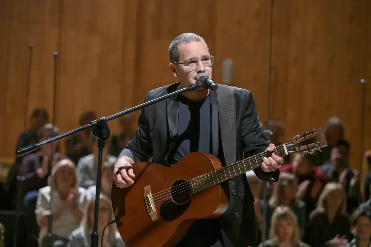 Artysta w okularach gra na gitarze podczas koncertu Męskie Granie. Publiczność w tle.