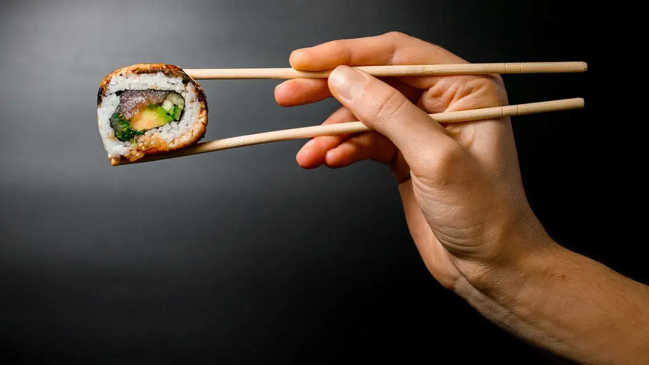 Dłoń trzyma pałeczkami jedno sushi. Zastanawiasz się, ile sushi na osobę będzie idealne na kolację?