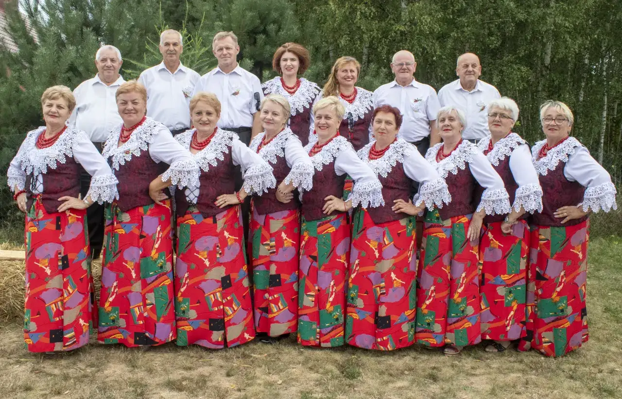 Grupa ludzi w strojach ludowych, kobiety w czerwonych korale i wzorzystych spódnicach, mężczyźni w białych koszulach. Kto śpiewa czerwona jarzębina?