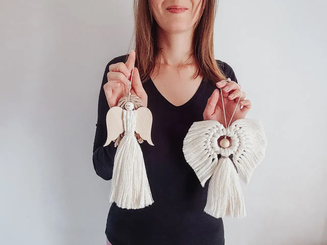 Kobieta prezentuje dwa anioły z makramy. Jeden z drewna, drugi w całości wykonany techniką makramy.