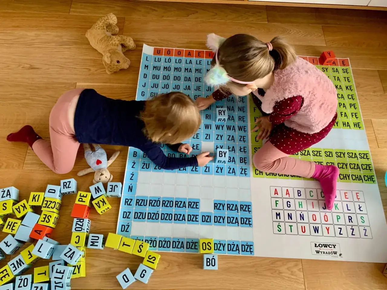 Dwie dziewczynki uczą się czytać, układając litery na planszy. Zabawa z literami wspiera naukę czytania.