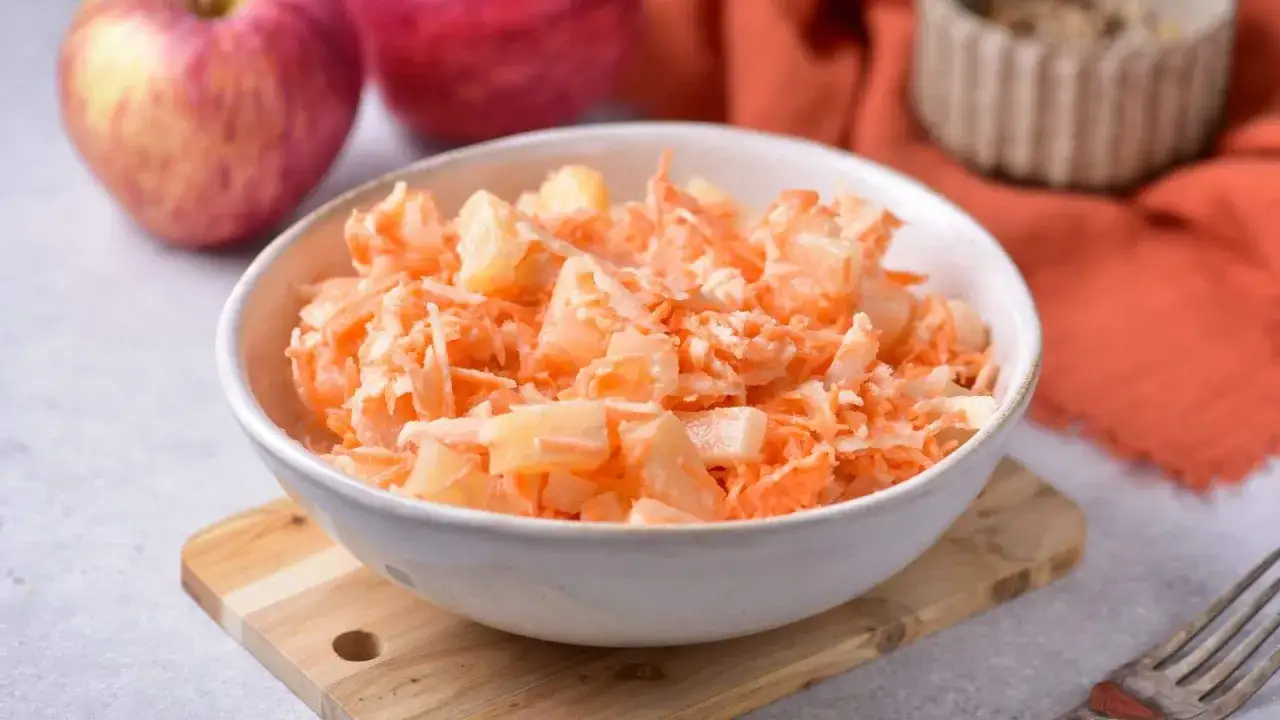 Miseczka z tartą marchewką i kawałkami ananasa, obok jabłka.