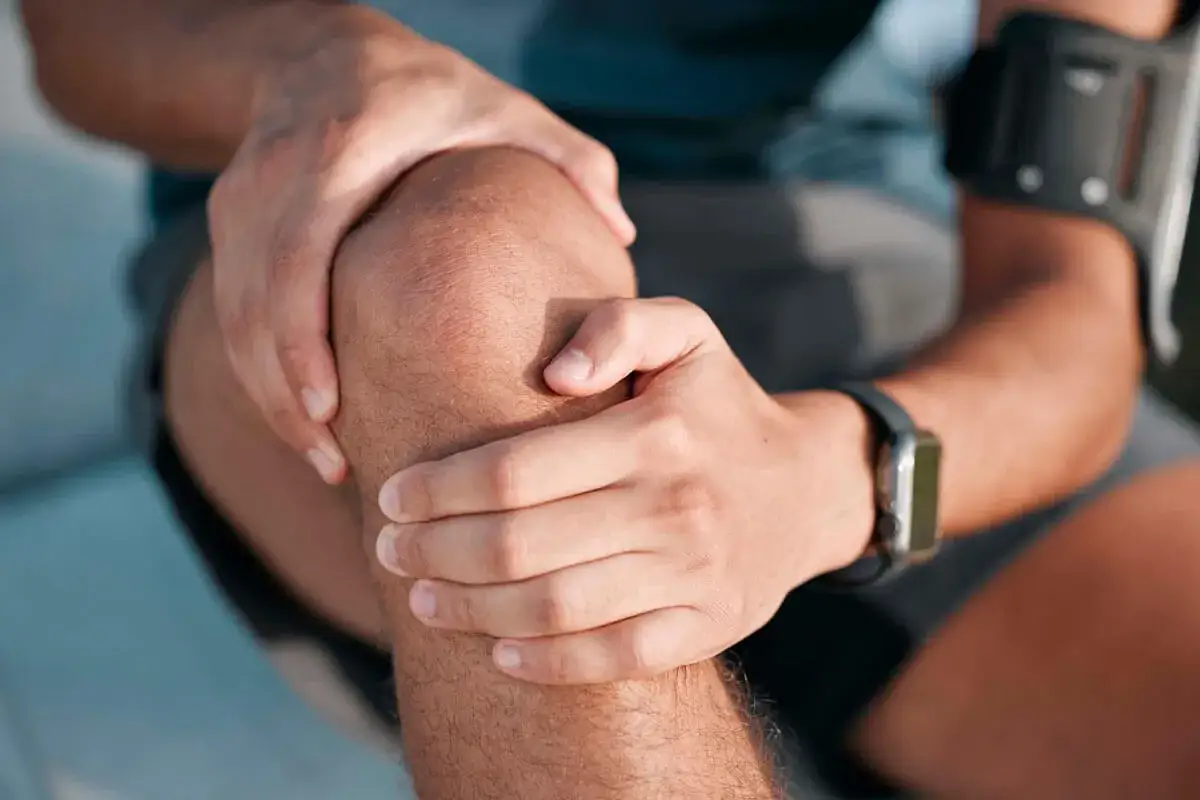 Mężczyzna trzyma się za kolano, zastanawiając się, jak długo trwa rehabilitacja po endoprotezie kolana.