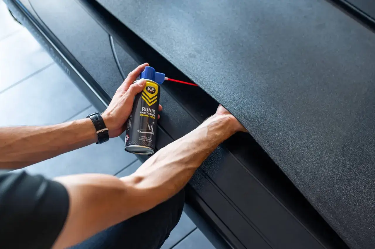 Dłoń trzymająca puszkę smaru do bieżni i aplikująca go pod pas.