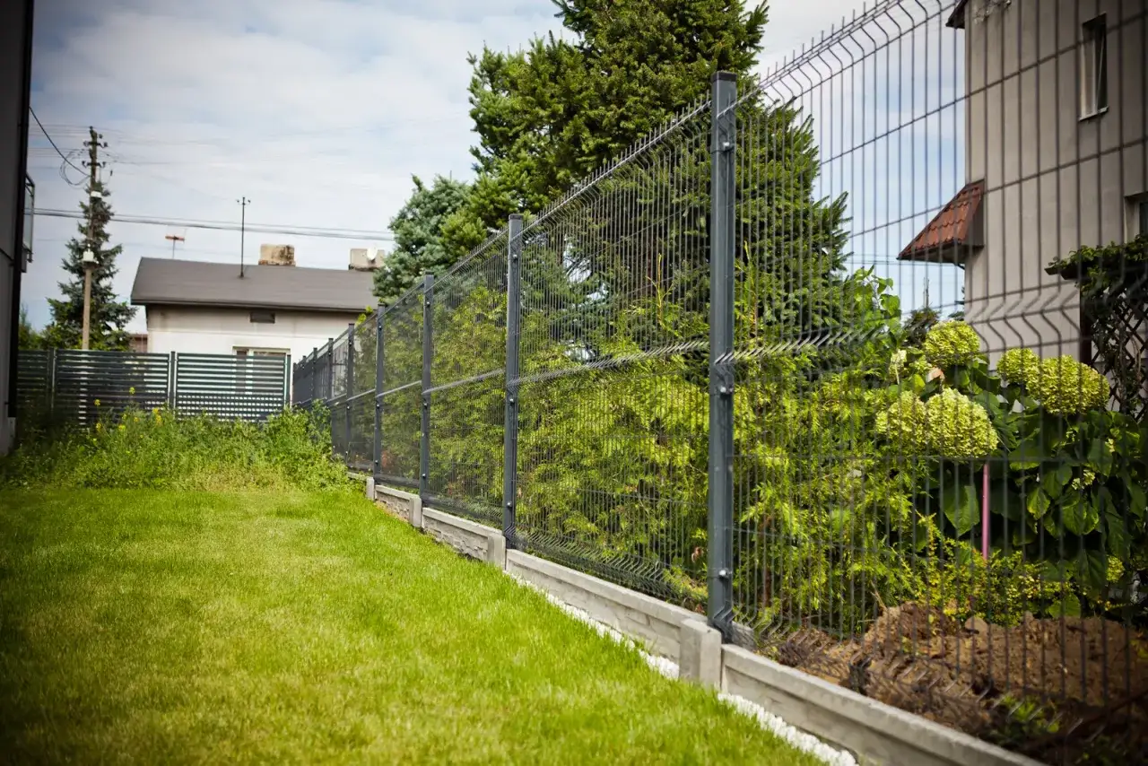 Ogrodzenie panelowe na pochyłym terenie z betonowym podmurówką i zieloną trawą.