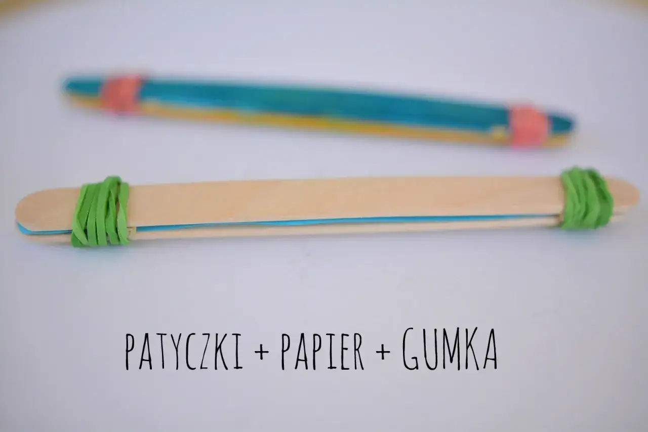 Proste instrumenty muzyczne do zrobienia: patyczki, papier i gumka. Dwa patyczki połączone gumkami, jeden z kolorowym papierem w środku.
