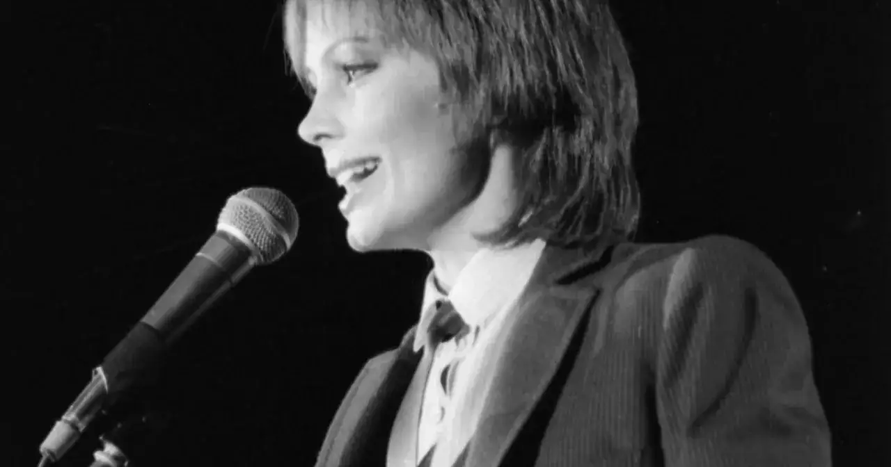 Kobieta śpiewa do mikrofonu, w garniturze i krawacie. Może to być scena z teledysku do piosenki "tekst piosenki wszystko czego dzis chce".