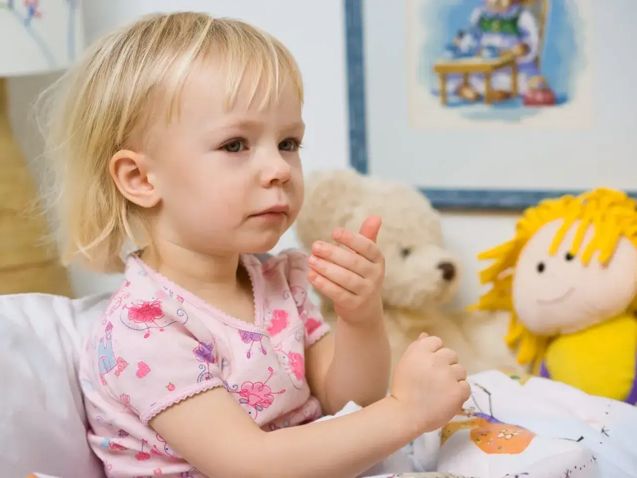 Mała dziewczynka w łóżku, otoczona pluszakami, może mieć zapalenie oskrzeli objawy.