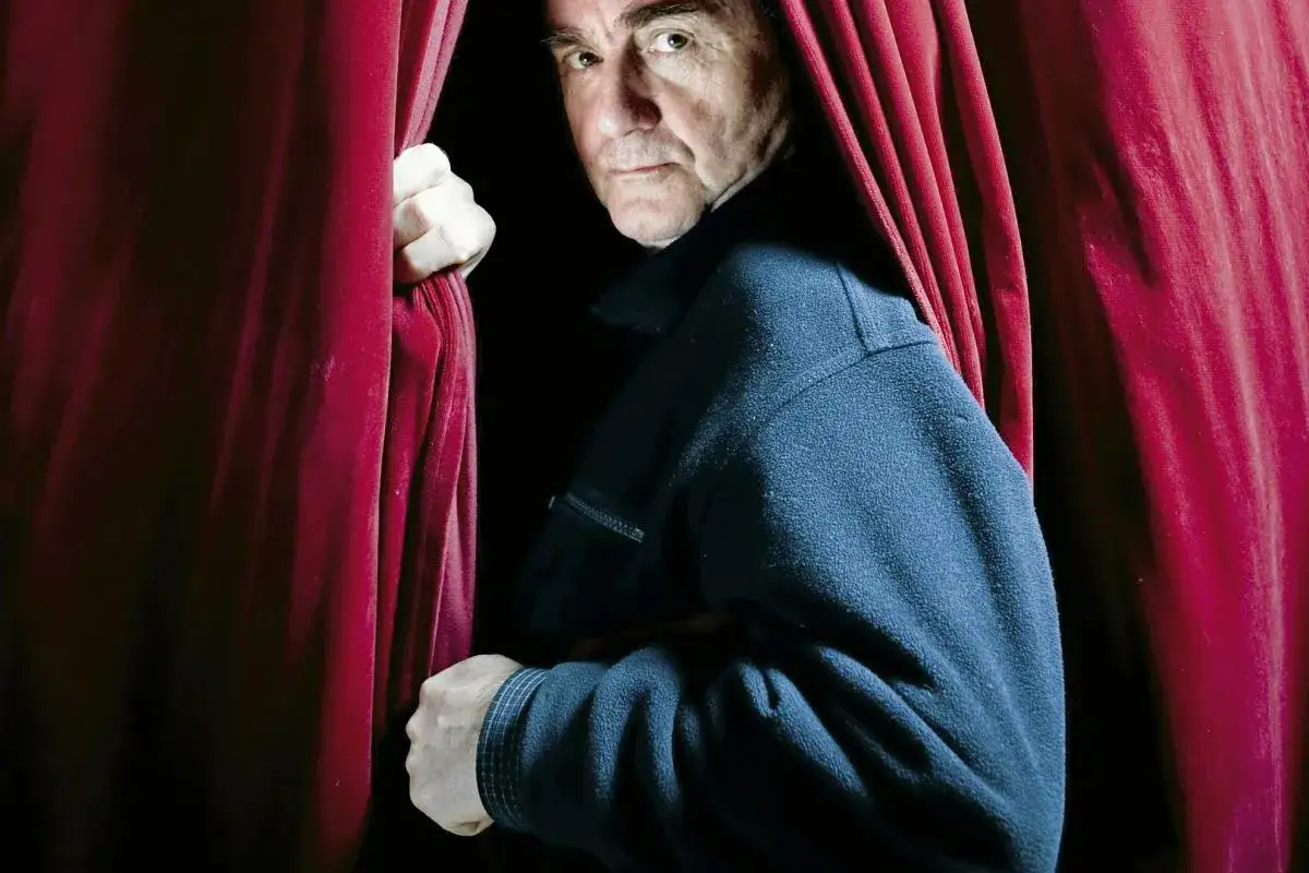 Jan Peszek młody, wychodząc zza czerwonej kurtyny, spogląda wprost na widza.