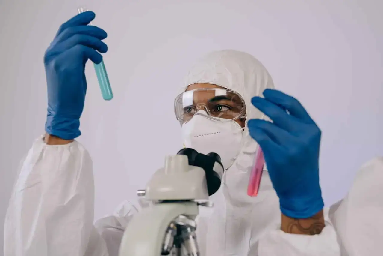 Badacz w kombinezonie i masce analizuje próbki w probówkach, przygotowując się do pracy w laboratorium chemicznym.