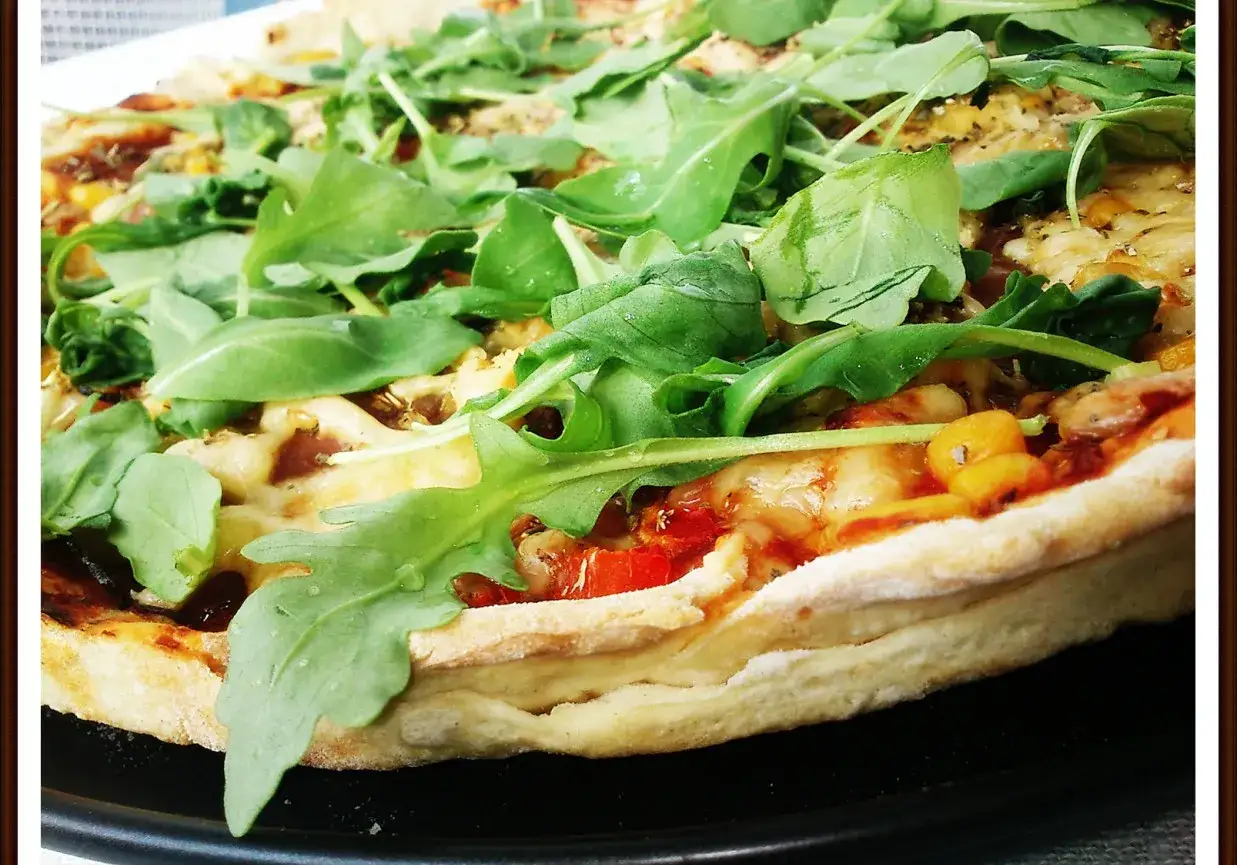 Pyszna pizza z rukolą, pomidorami i serem, pachnąca ziołami. Idealna na szybki obiad.