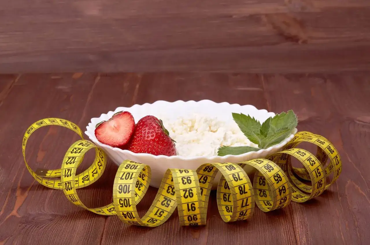 Twarożek z truskawkami i miętą, otoczony miarką krawiecką. Idealne śniadanie, gdy zastanawiasz się, ile kalorii na śniadanie przy odchudzaniu.