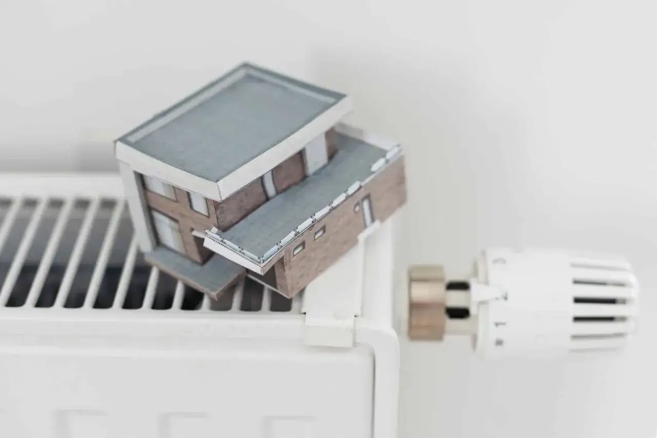 Model domu na grzejniku symbolizuje wysokie koszty ogrzewania i potrzebę dopłat do prądu.