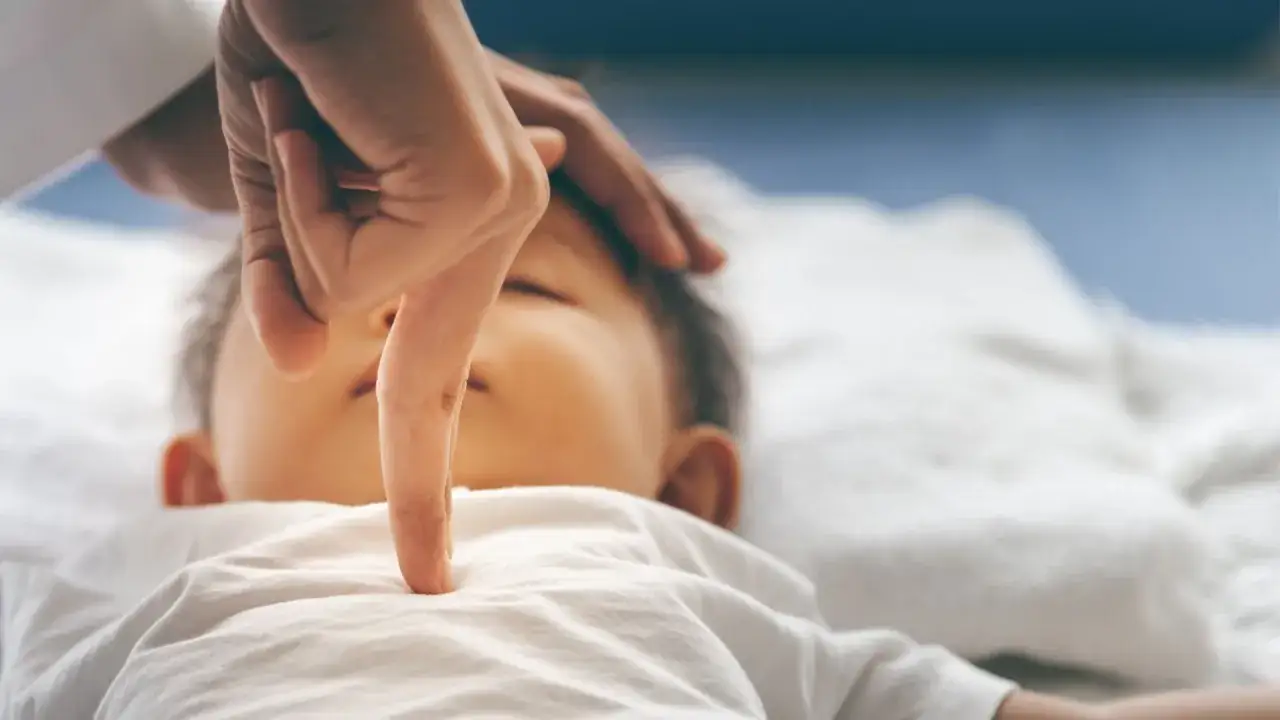 Dłoń lekarza bada klatkę piersiową śpiącego dziecka.