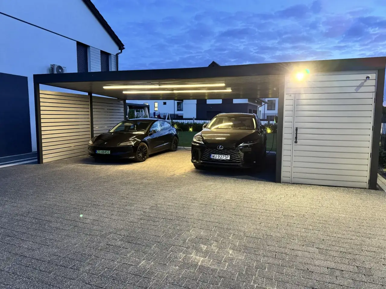 Nowoczesna wiata na 2 samochody projekt. Dwa czarne auta, Tesla i Lexus, stoją pod zadaszeniem z oświetleniem LED.