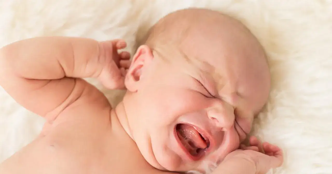 Noworodek płacze z otwartymi ustami i zamkniętymi oczami na białym tle.