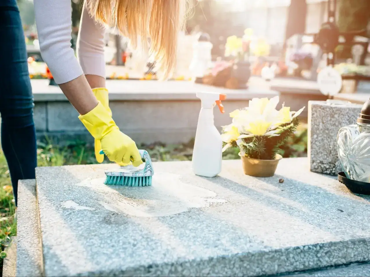 Kobieta w żółtych rękawiczkach czyści szczotką granitowy pomnik.