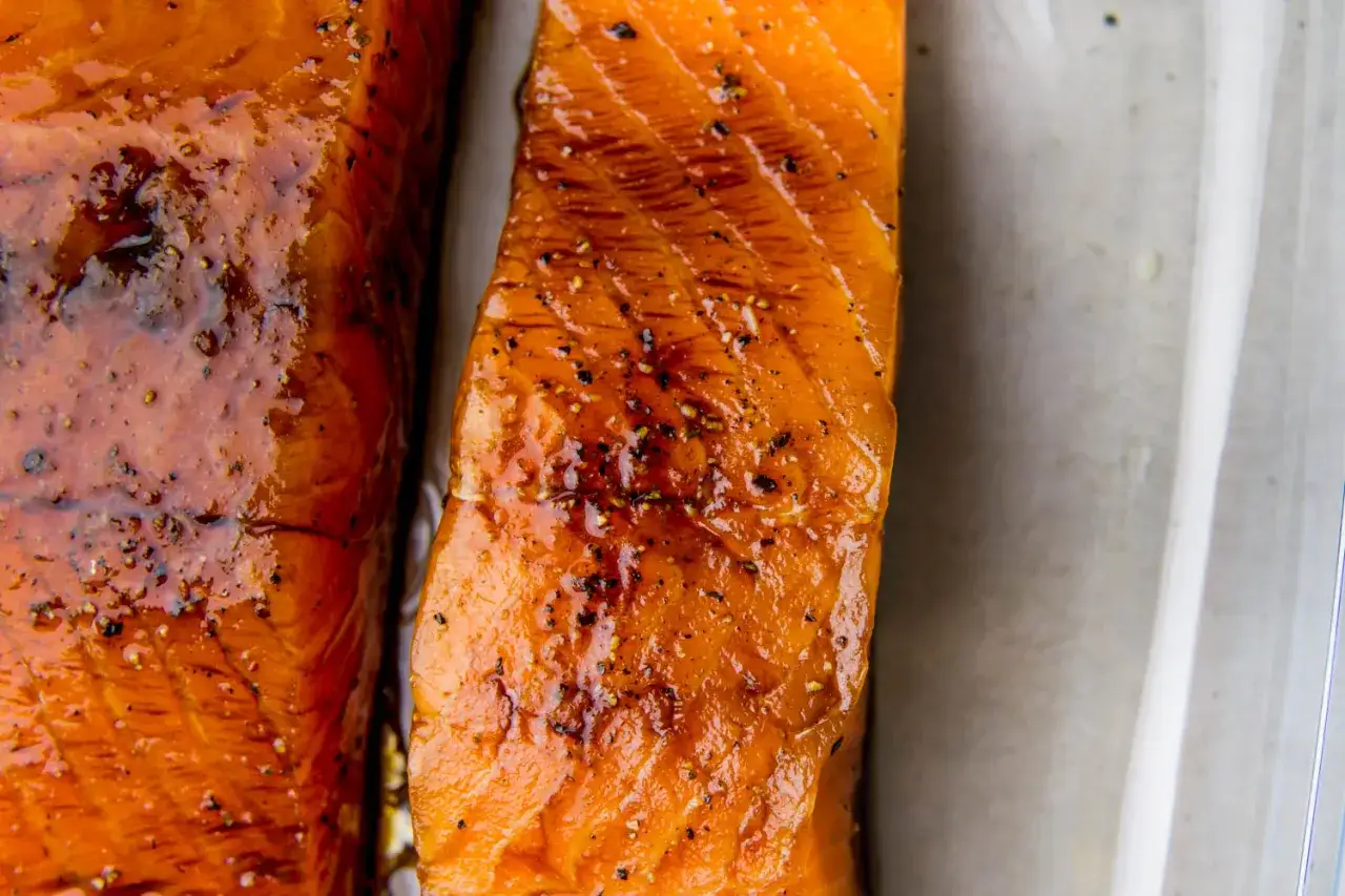 Dwa kawałki soczystego łososia w sosie sojowym, błyszczące i doprawione pieprzem, gotowe do podania.