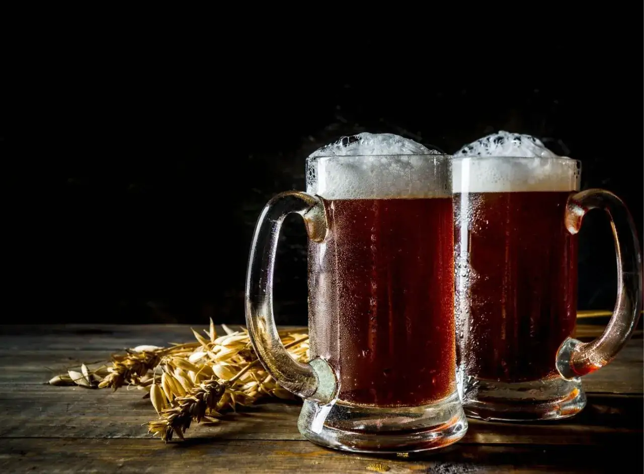 Dwa kufle ciemnego piwa z pianką, obok kłosy zboża. Zastanawiasz się, ile może stać otwarte piwo?