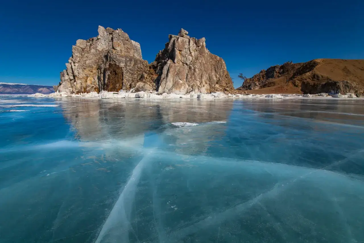 Skaliste formacje na zamarzniętym, błękitnym jeziorze Bajkał pod błękitnym niebem.