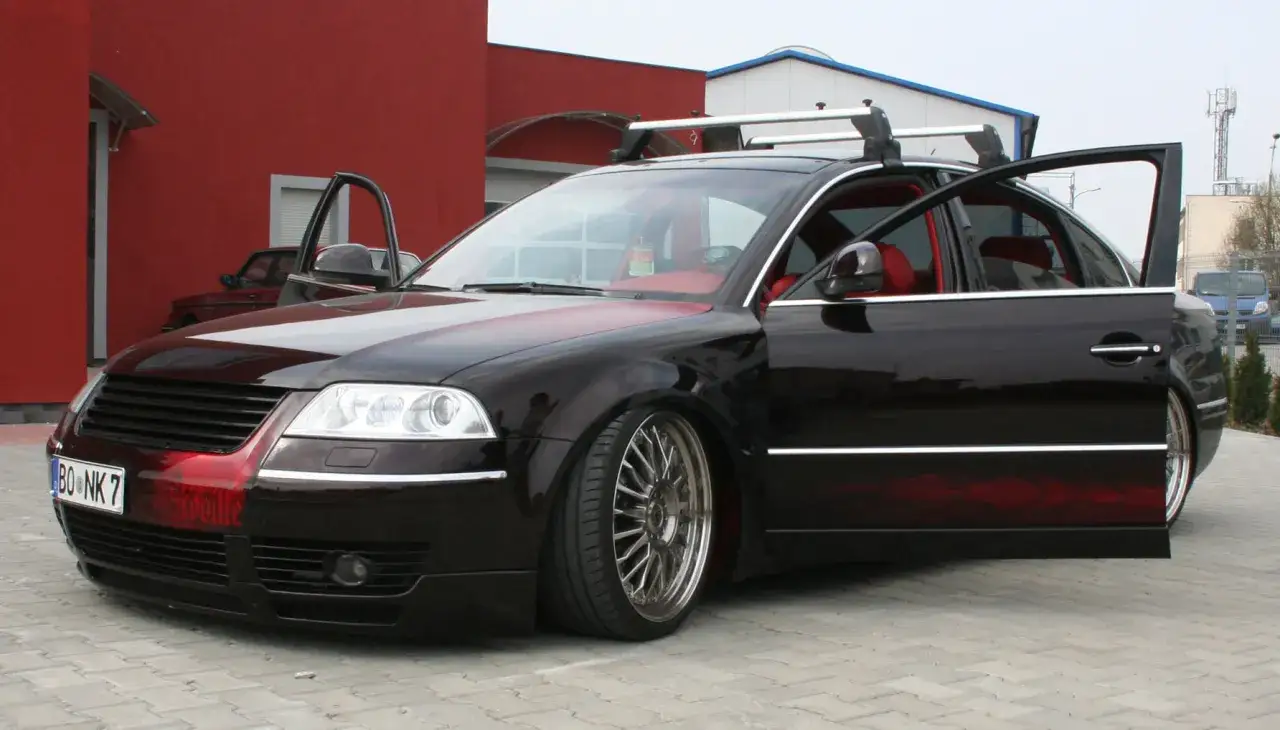 Czarny Passat B5 z body kitem i czerwonymi wstawkami, otwarte drzwi, czerwone wnętrze, relingi dachowe.