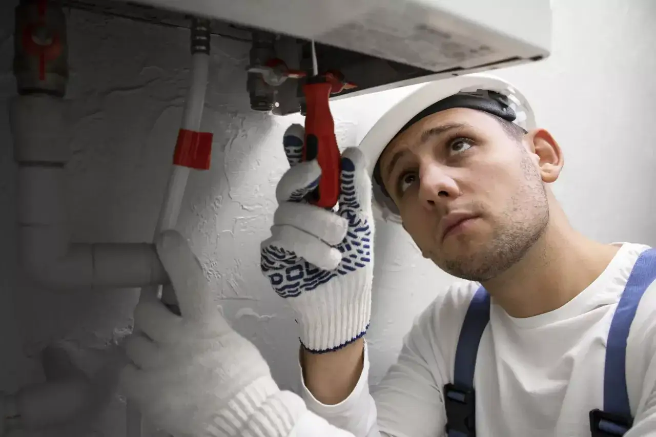 Instalator w białej rękawicy dokręca śrubę przy bojlerze.