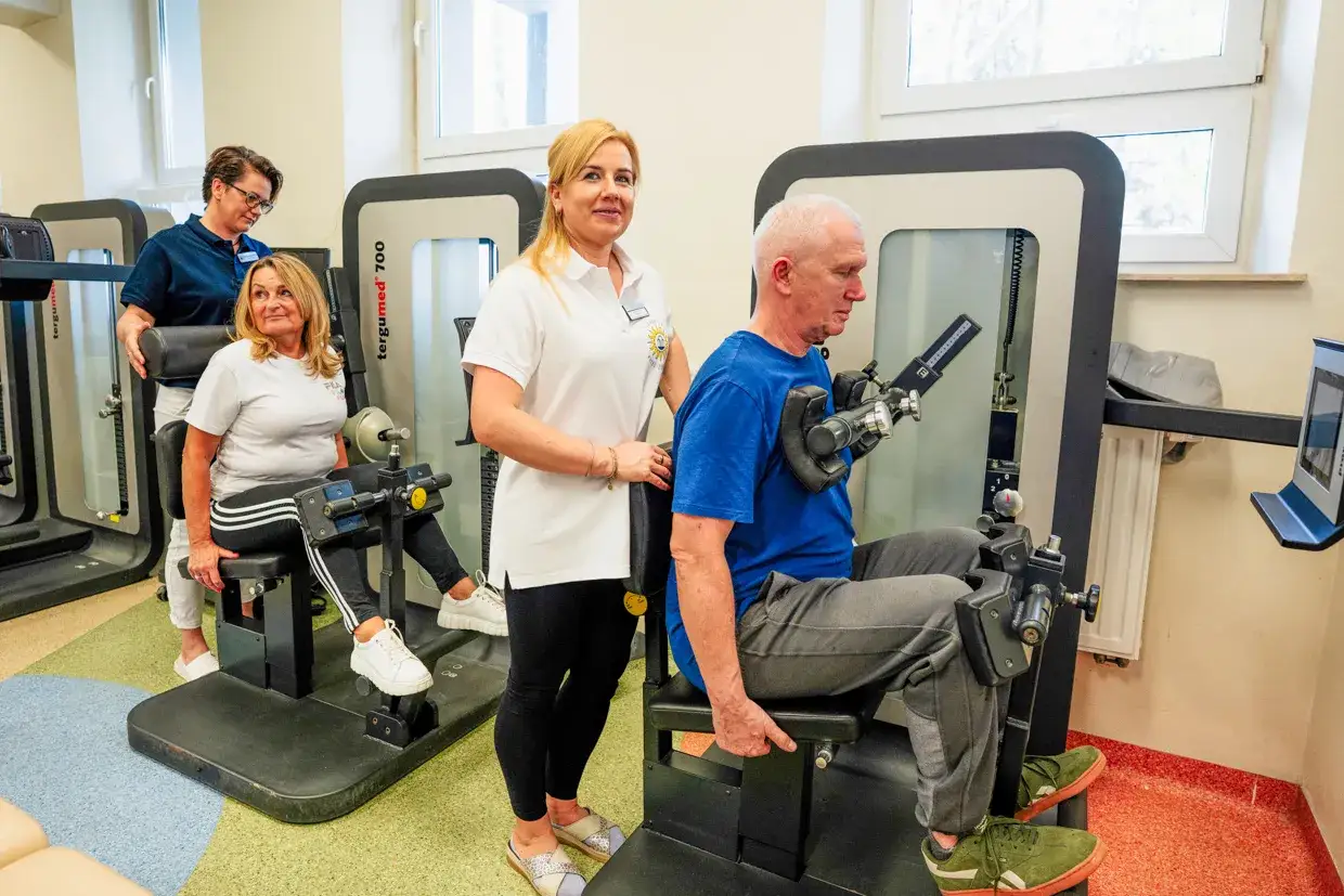 Rehabilitacja w Busko Zdrój: pan ćwiczy na siłowni pod okiem fizjoterapeutki, a pani z pomocą drugiej terapeutki. Sprawdź nasze sanatoria Busko Zdrój promocje!
