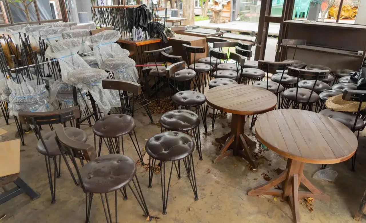Viele gebrauchte Gastrostühle und runde Holztische stehen in einem Raum.